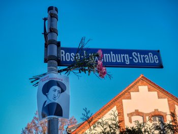 Straßenschild der Cottbusser Rosa-Luxemburg-Strasse mit Blumen anläßlich Rosas Geburtstag geschmückt.